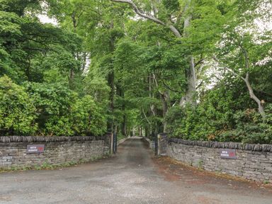 A driveway through trees with stone walls and signs reading Bryn Derwen at Bryn Derwen Lodge in Bethesda