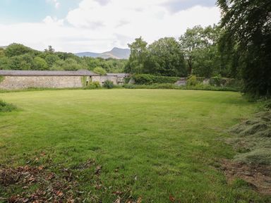 A wide grassy lawn with trees and stone walls in the background at Bryn Derwen Lodge in Bethesda