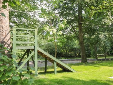 A wooden zipline platform with a ramp in a grassy yard surrounded by trees at Bryn Derwen Lodge in Bethesda