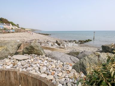 A rocky beach with large boulders and pebbles near the sea and houses along the coastline at Covert Farm Cwtch in Jeffreyston