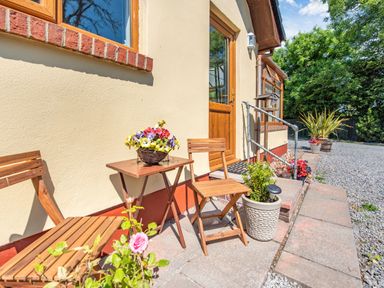 A small outdoor patio with wooden chairs and a table with flowers near a house entrance at Covert Farm Cwtch in Jeffreyston