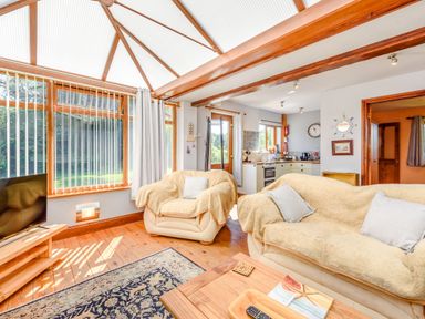 A living room with beige sofas and a wooden floor next to a kitchen and large windows at Covert Farm Cwtch in Jeffreyston