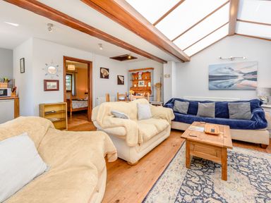 A living room with sofas a wooden coffee table a dining table and a painting on the wall at Covert Farm Cwtch in Jeffreyston