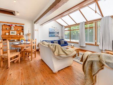 A living room with wooden chairs and table a wooden cabinet and sofas with blankets at Covert Farm Cwtch in Jeffreyston