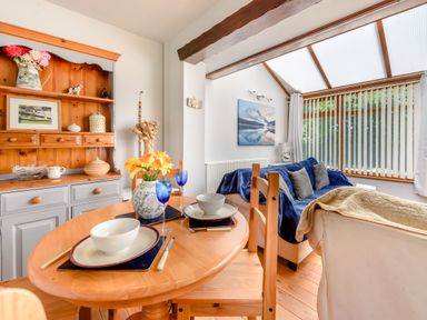 A dining area with a wooden table set for two and a living area with chairs and sofa under a skylight at Covert Farm Cwtch in Jeffreyston