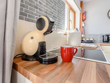 A kitchen counter with a coffee machine and red mug near a window at Covert Farm Cwtch in Jeffreyston