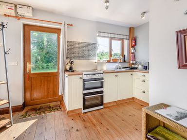 A kitchen with wooden floor cabinets an oven a coffee machine and a window overlooking greenery at Covert Farm Cwtch in Jeffreyston