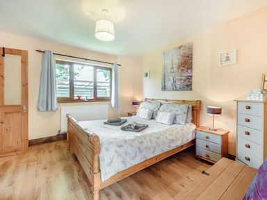 A bedroom with a wooden bed and grey bedding beside a window with curtains at Covert Farm Cwtch in Jeffreyston