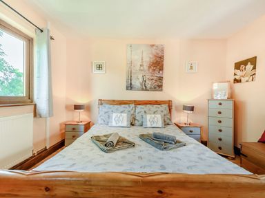 A bedroom with a wooden bed frame bedside tables with lamps and a chest of drawers at Covert Farm Cwtch in Jeffreyston