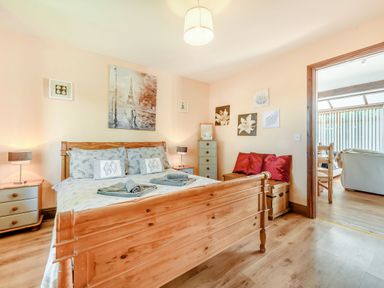A bedroom with a wooden bed and nightstands next to a doorway showing a sitting area at Covert Farm Cwtch in Jeffreyston