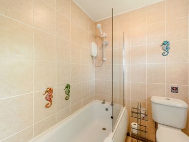 A bathroom with a bathtub shower combination a glass shower screen a toilet and seahorse decorations on tiled walls at Covert Farm Cwtch in Jeffreyston