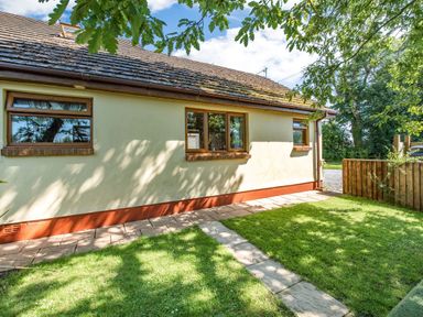 A side view of a house with three windows a tiled roof a paved walkway and a grassy yard at Covert Farm Cwtch in Jeffreyston