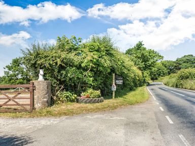 A country road with greenery and a wooden gate with a stone post and a camping sign at Covert Farm Cwtch in Jeffreyston
