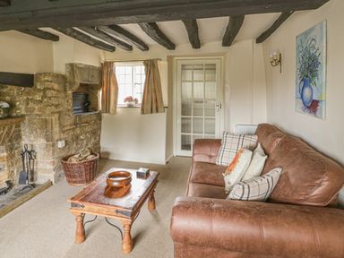 A living room with a brown leather sofa cushions a wooden coffee table a stone fireplace and wooden ceiling beams at Spring Cottage in Alkerton near Banbury