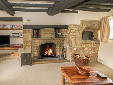 A living room with a stone fireplace a wooden coffee table and a television at Spring Cottage in Alkerton near Banbury