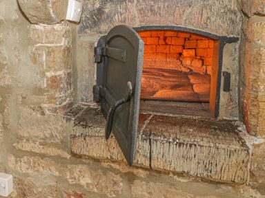 An open brick oven with a black metal door built into a stone wall at Spring Cottage in Alkerton near Banbury