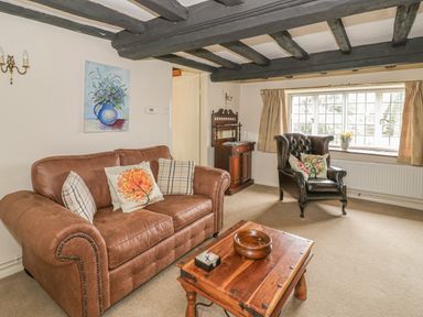A living room with a brown leather sofa, a black armchair, a wooden coffee table, and a window with beige curtains at Spring Cottage Alkerton near Banbury