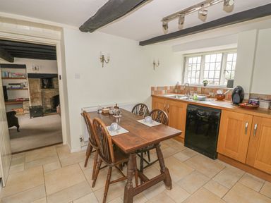 A kitchen with a wooden dining table and chairs wooden cabinets a black dishwasher and a window at Spring Cottage Alkerton near Banbury