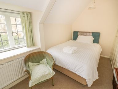 A small bedroom with a double bed next to a window and a wicker chair with a cushion at Spring Cottage in Alkerton near Banbury