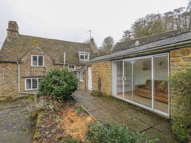 A stone courtyard with plants and patio in front of a stone house with sliding glass doors at Spring Cottage in Alkerton near Banbury