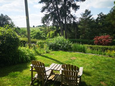 A garden with two wooden chairs and a small table on grass surrounded by trees and bushes at Spring Cottage in Alkerton near Banbury