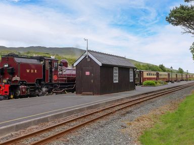 A steam train at a station with a wooden shed at Sygun View Beddgelert
