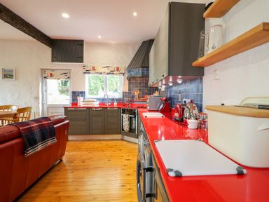 A kitchen with red countertops wooden floor grey cabinets and a red sofa at Quiet Waters Cottage in Loughan near Coleraine