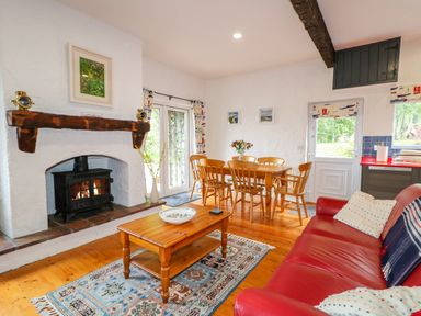 A living room with a red sofa wooden coffee table rug fireplace and dining table at Quiet Waters Cottage in Loughan near Coleraine