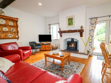 A living room with red leather sofas a wood burning stove a wooden coffee table and television at Quiet Waters Cottage in Loughan near Coleraine