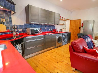 A kitchen with red countertops gray cabinets and appliances next to a red sofa at Quiet Waters Cottage in Loughan near Coleraine