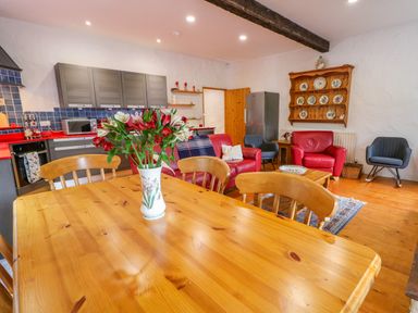 A kitchen and living area with wooden dining table flowers on table red and gray chairs wooden floor at Quiet Waters Cottage Loughan near Coleraine