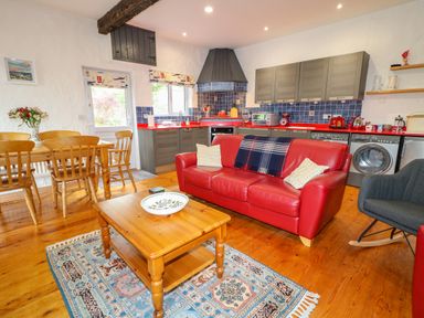A kitchen and living area with a red sofa wooden dining table and chairs a wooden coffee table and kitchen cabinets at Quiet Waters Cottage in Loughan near Coleraine