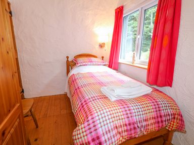 A bedroom with a single bed and a checkered bedspread next to a window with red curtains at Quiet Waters Cottage in Loughan near Coleraine