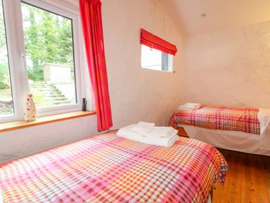 A bedroom with two single beds with checkered bedding and folded towels next to windows with red curtains at Quiet Waters Cottage in Loughan near Coleraine