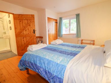 A bedroom with a bed with blue patterned bedding towels on bed wooden doors and a window with curtains at Quiet Waters Cottage in Loughan near Coleraine
