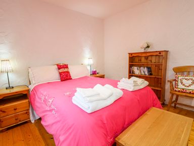 A bedroom with a double bed with pink bedding wooden bedside tables and a wooden bookshelf at Quiet Waters Cottage in Loughan near Coleraine