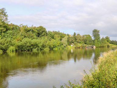 A river with trees along the banks and a small dock in the background at Quiet Waters Cottage in Loughan near Coleraine
