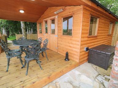 A wooden outdoor deck with metal table and chairs beside a wooden cabin at Quiet Waters Cottage Loughan near Coleraine