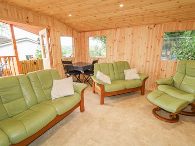 A wooden room with green leather sofas a matching armchair and a table with black chairs at Quiet Waters Cottage in Loughan near Coleraine
