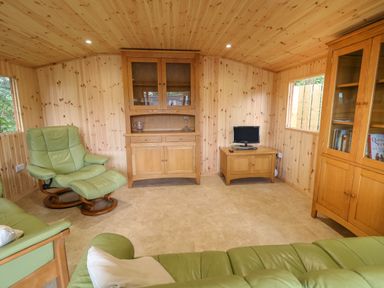 A wooden paneled room with green leather chairs a small TV on a wooden cabinet and wooden cupboards at Quiet Waters Cottage in Loughan near Coleraine