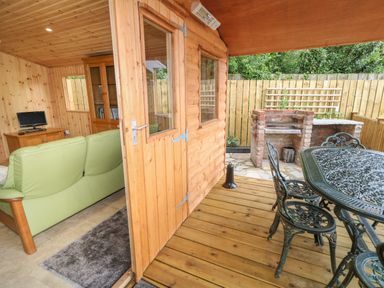A wooden cabin with a green sofa inside a room and an outdoor patio with a metal table and chairs and a brick barbecue at Quiet Waters Cottage in Loughan near Coleraine