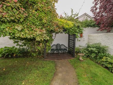 A garden with a paved path leading to a metal bench under a pergola covered with plants at Quiet Waters Cottage in Loughan near Coleraine