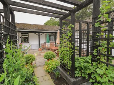 An outdoor garden area with trellises and climbing plants and a patio with tables and chairs at Quiet Waters Cottage in Loughan near Coleraine