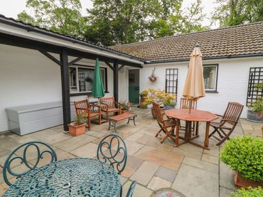 A patio with wooden chairs and tables with umbrellas and potted plants at Quiet Waters Cottage in Loughan near Coleraine