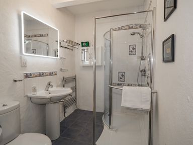 A bathroom with a shower, sink, toilet, illuminated mirror, towel rack, and first aid kit at Quiet Waters Cottage in Loughan near Coleraine