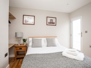 A bedroom with a bed two pillows bedside table lamp plant two pictures on the wall and a door at Laneton in Rhosneigr