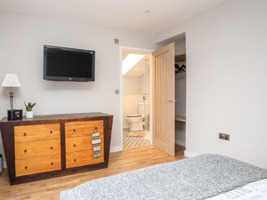 A bedroom with a wooden dresser a wall-mounted TV an open door showing a bathroom and a partially open closet at Laneton in Rhosneigr