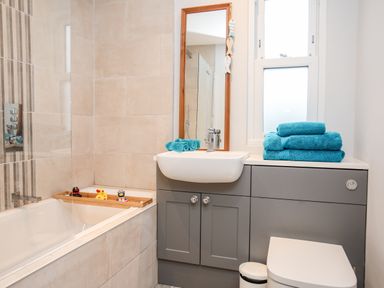 A bathroom with a bathtub containing rubber ducks a sink with a mirror above folded towels on the countertop and a toilet at Laneton in Rhosneigr