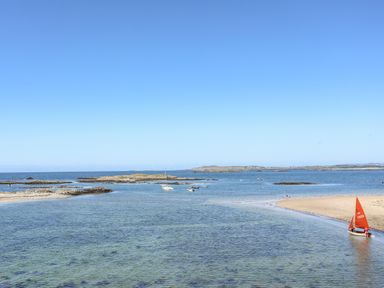 A coastal scene with a sandy beach and people with a small red sailboat on the shore at Laneton in Rhosneigr