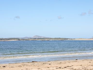A sandy beach with gentle waves and a distant view of hills and sparse clouds at Laneton in Rhosneigr